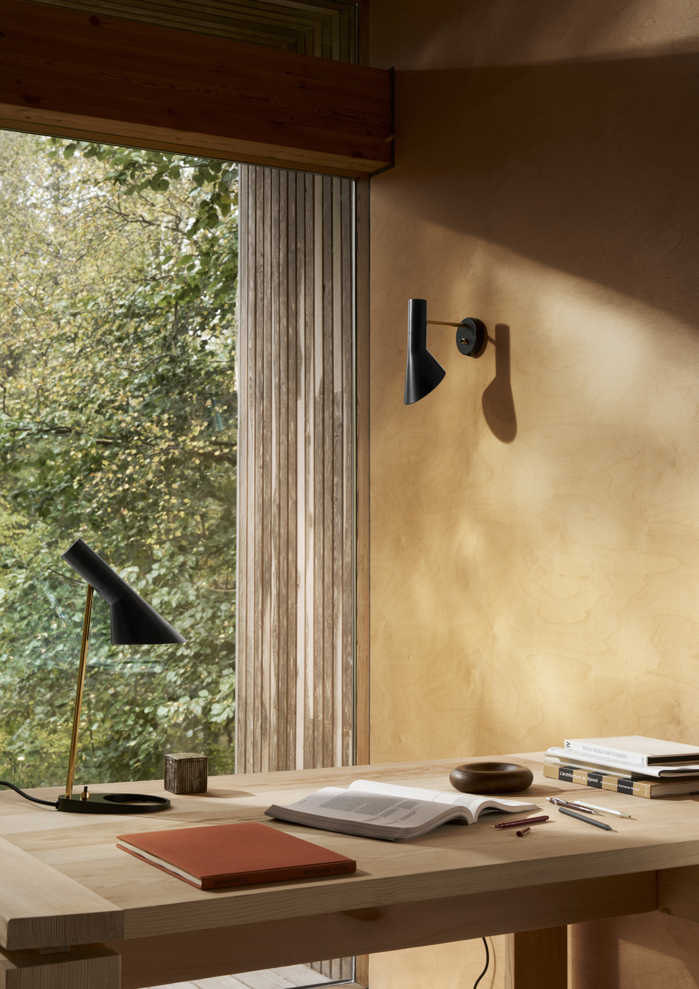AJ Wall lamp in black with brass details mounted on a light wooden wall, complemented by an AJ Mini Table lamp, © 2025 Louis Poulsen.